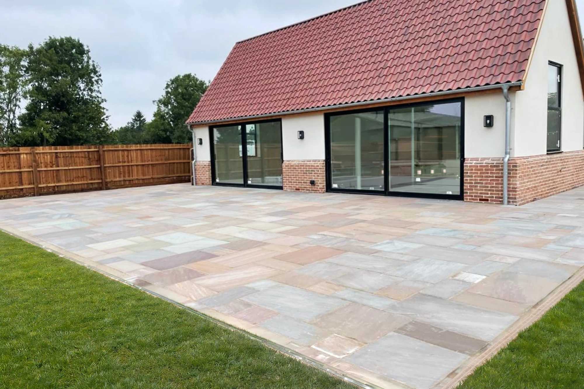 Newly installed natural stone patio at a modern residential property with expansive outdoor paving, glazed doors and neat lawn edges.