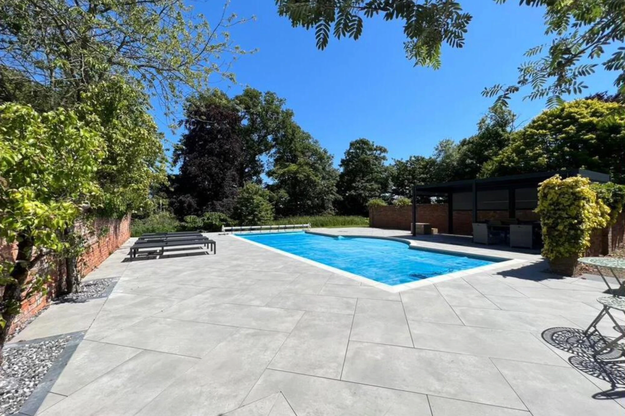 Contemporary porcelain paving installed around a private outdoor swimming pool with clean lines, terrace seating and a modern garden setting.